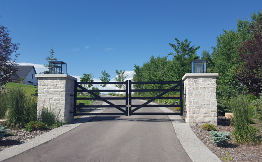 Calgary, Alberta, Canada- July 16,2022:  Large gate across driveway that leads up to home. Stone pillars on either side. Xeriscaped landscaping at side of gate and driveway.