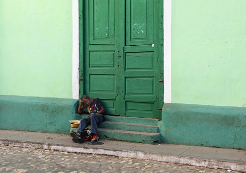 Trinidad, Cuba, December 6, 2017: A man rests on the steps of a house in Trinidad. The historic district of the town is listed as UNESCO World Heritage Site.