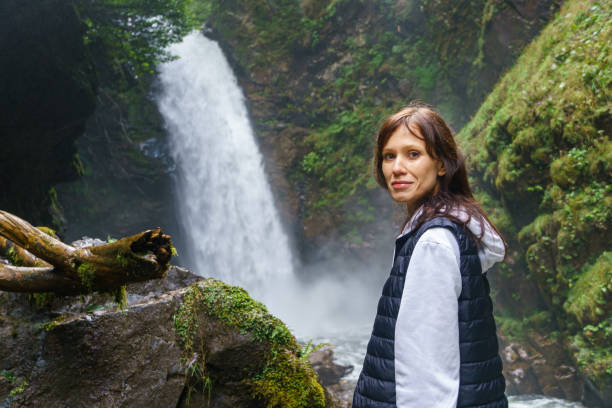 istock Young woman standing in front of waterfall 1410489851