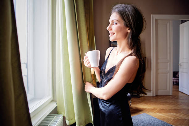 portrait d’une jeune femme regardant par la fenêtre le matin - joy the human body smiling women photos et images de collection