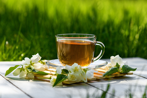 Jasmine tea in glass cup and flowers on a wooden white background, natural light photo. Cup with green jasmin tea