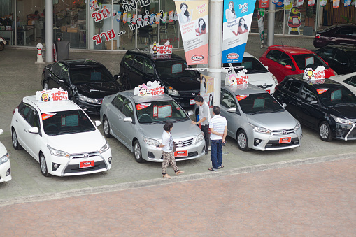 Some thai people are inspecting Toyota vehicles at car dealer's shop at Ratchadaphisek Road in Bangkok Chatuchak. View from footbridge dow to sidewalk and dealer's shop. At cars are sales signs