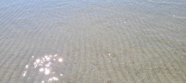 Lines in the sand submerged in ocean water with glare from the sun on a clear day