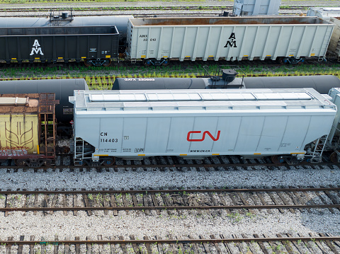 A new CN Rail hopper train car with the Canadian National Railway logo on it is seen from a close-up low aerial view while it is stationary in a railyard in Hamilton, ON, Canada, during the day.
