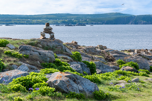 An inukshuk stands proudly on the rocky shore of Elliston, near Bonavista, Newfoundland during early sunset.