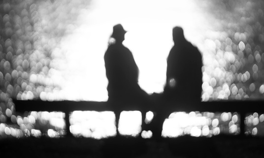 Silhouettes of  romantic back lit elderly couple on bench