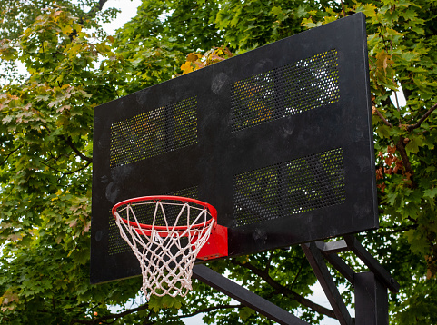 A red hoop on a black metal backboard on a basketball court in a park.