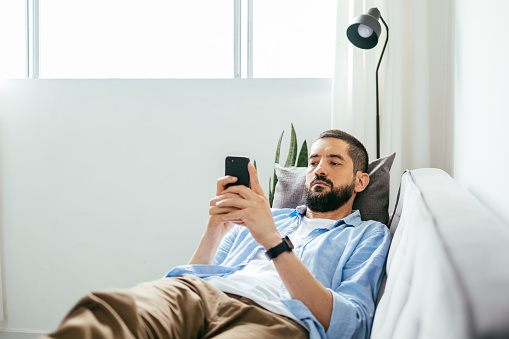 Young brazilian man lying on sofa using smartphone