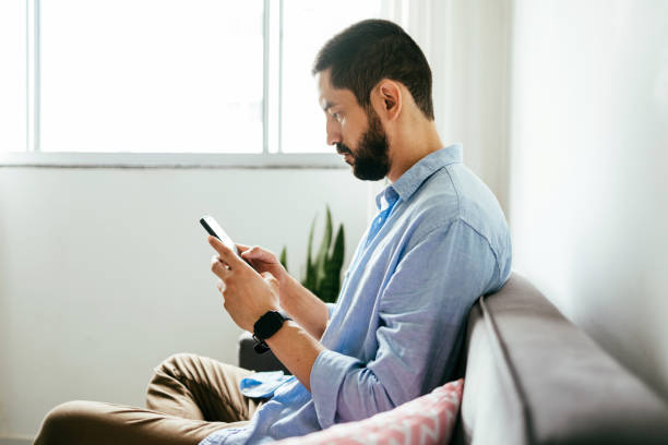 istock Young brazilian man sitting on sofa using smartphone 1410520279