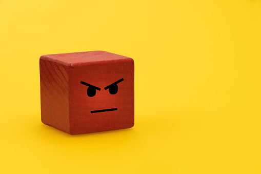 Anger and frustration, Creative concept, Outbursts of anger, therapy helping to deal with negative emotions, Red wooden block with painted human feelings, Yellow background, empty space