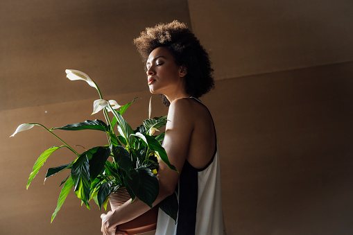 A pensive African-American female standing outdoors and enjoying taking care of her plant.