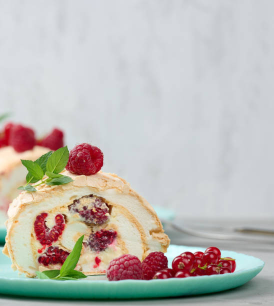 istock Baked meringue roll with red berries on a round plate, white background 1410524273