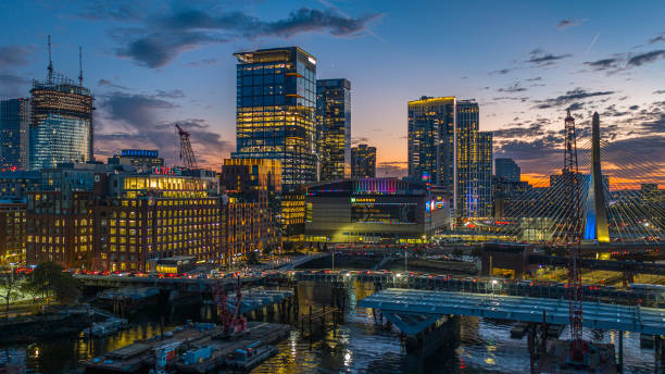 ponte zakim sul fiume charles al crepuscolo. illuminato lo skyline della città di boston con edifici moderni in costruzione. - boston charles river skyline massachusetts foto e immagini stock