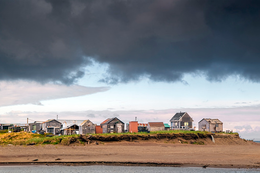 Fishing shacks along the bank of the Nome River with a brooding sky in Nome, Alaska.