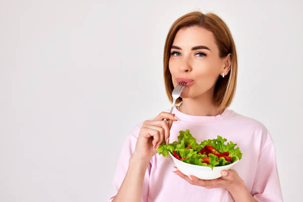 istock beautiful woman eating fresh vegetable salad on white background 1410536558