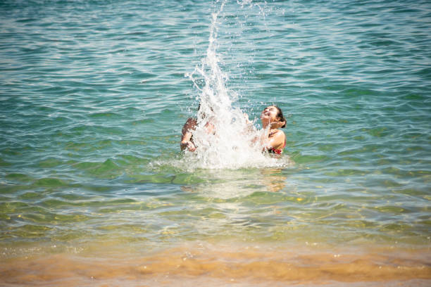 Two women splashing water on the beach at Porto da Barra in Salvador, Bahia.