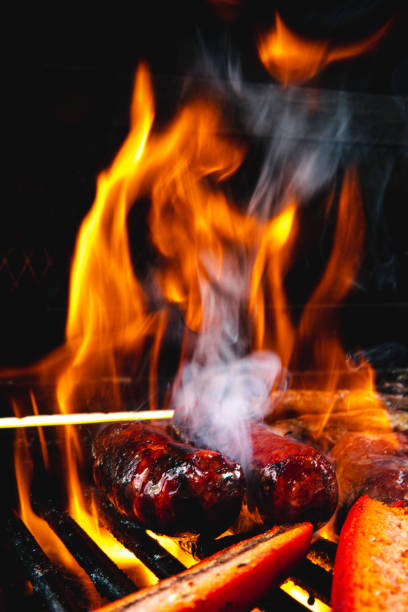 Whole and cut sausages on the grill. The background of the black images. The fire is very high and you can see the smoke coming out.
