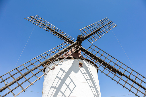 A view of the blades of a windmill silhouetted against the blue sky and sunlight in the Castilian village of Consuegra in Toledo, Spain.