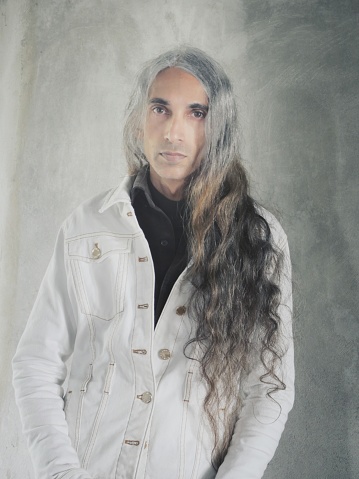 Man with long hair standing and looking at camera in front of gray background