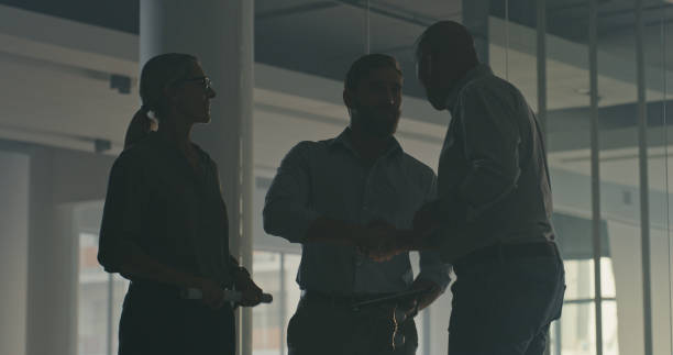 Silhouette of three people inside a dark empty office building or warehouse. Low angle of unrecognizable workers and manager standing, planning remodel layout or discussing construction