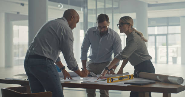 istock Architects analyzing building plans for a construction project. Group of focused designers and civil engineers collaborating to discuss and brainstorm a layout for a commercial property development 1410570584