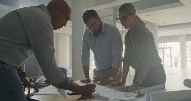 istock Team of architects working on a project together in the office. Group employees designing a building structure at a modern workplace. Business people drafting and drawing a plan for a home 1410571903