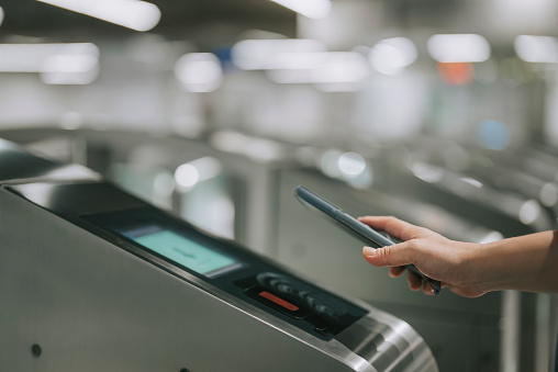 Asian chinese woman paying with her smart phone at subway station entrance