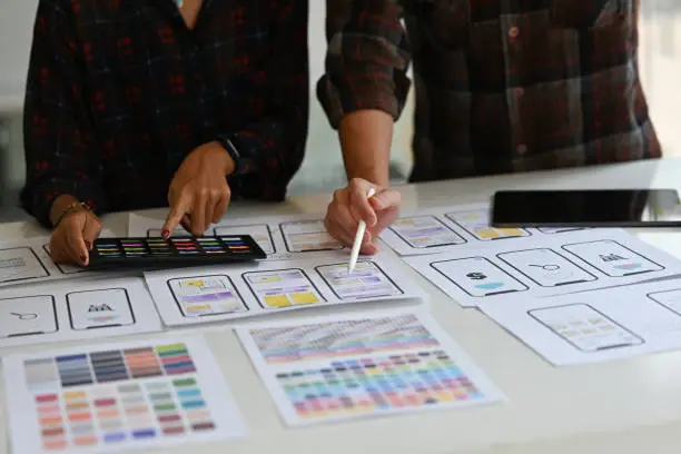 Photo of Close up Creative Ux developer and Ui designer brainstorming about mobile app interface wireframe design on table with customer brief and color code.