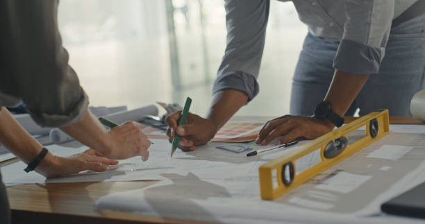 istock Business people drawing up a construction plan on paper at work. Creative architects brainstorming and planning a renovation design using a blueprint. Designers working on a detailed picture for job 1410574059