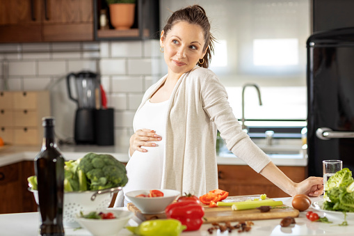 Pregnant woman in the kitchen prepare healthy vegetarian food  and smile