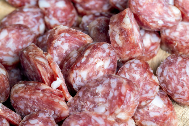sliced thin sausage with bacon on a wooden dish, sliced pork sausage and other ingredients on the table