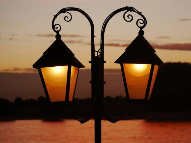 istock Wrought-iron lantern illuminated, as a silhouette in front of the sky illuminated by the sunset in the blurred background. Enough space on the windows of the lantern to insert your own text. 1410589983