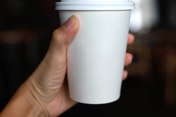 istock Close up hand holding a white coffee paper cup mockup with bokeh background 1410592610