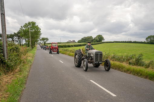 An old farmer driving a vintage looking grey tractor being followed by other vintage tractors

On July 13  2022, The  Peninsula Vintage Club held a Tractor Run on The Ards Peninsula starting and ending at the Kirkubbin Sailing Club.

This image was made outside the seaside village of Ballywalter, Newtownards, County Down, Northern Ireland. It shows a male farmer driving on a Northern Ireland, country road.

Tractor Runs are a very popular way of raising cash for charities in Northern Ireland as well maintaining these old vehicles for future generations.