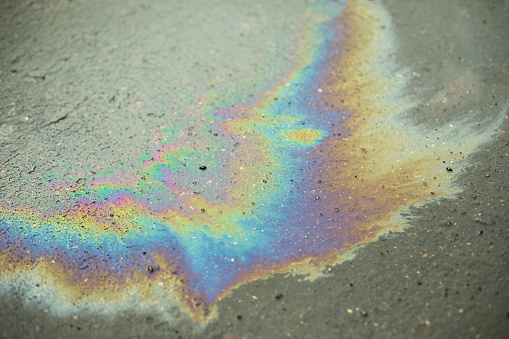 A stain of gasoline on the asphalt. Trace of spilled fuel. All colors in combustible liquid.