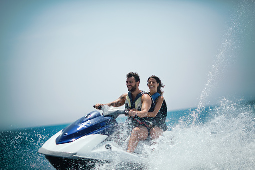 Young couple jet skiing on the open sea. They are smiling and enjoying summer sport on water.