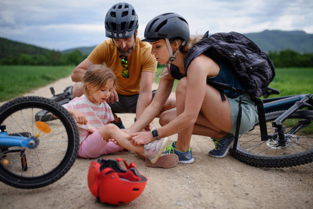 mother and father helping their little daughter after falling off bicycle outdoors - child bicycle cycling danger imagens e fotografias de stock