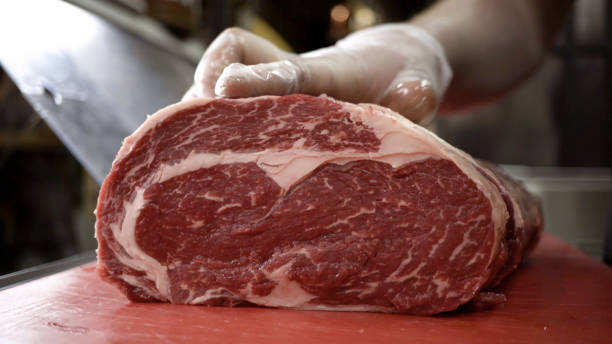 açougueiro de luvas corta carcaça de carne vermelha. ação. close-up de faca profissional cortando enorme pedaço de carne em açougue - animal morto - fotografias e filmes do acervo