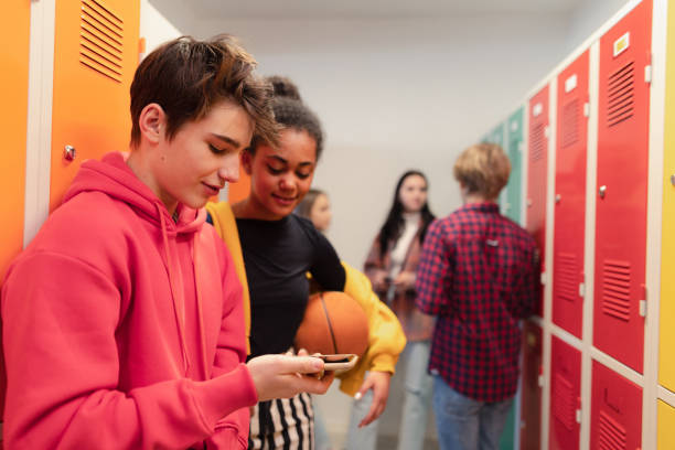 istock Young high school students standing near locker in campus hallway talking and using smartphone. 1410611547