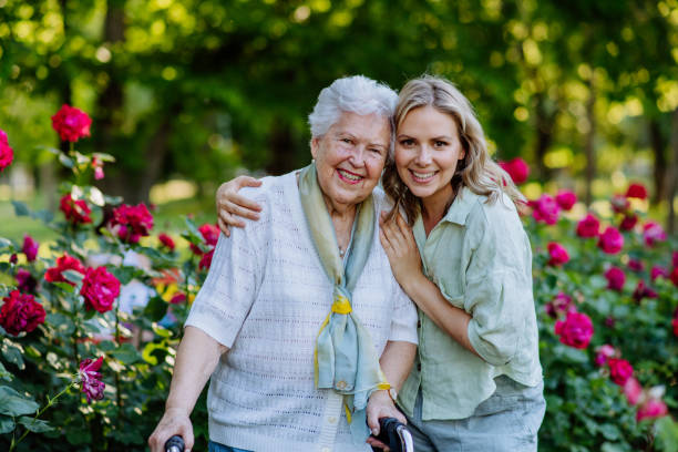 ritratto di nipote adulta con nonna anziana a piedi nel parco, con rose sullo sfondo - nipote femmina foto e immagini stock