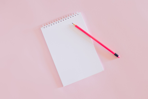 Notebook with blank page and pencil on pink background.
