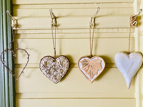 Horizontal still life of rustic wooden design heart shaped craft wall hangings in various designs on hooks against wood wall