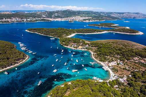 Island Marinkovac as part of Paklinski islands with its beach a many anchored sailing boats and yachts seen and captured from a helicopter during one busy summer day on the Adriatic Sea.