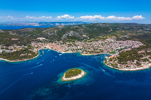Hvar old town and port on the island of Hvar, part of Split-Dalmatia County, Croatia, seen from a drone point of view during a summer season with many boats and yachts around it on the Adriatic Sea.