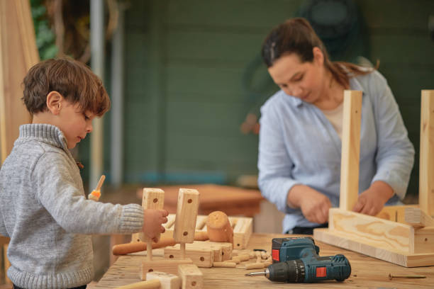 istock Mom doing fun activity with son in her free time, bonding and teaching him the craft of building toy objects out of wood with a drilling tool or equipment. Kid with parent assembling wooden birdhouse 1410621095