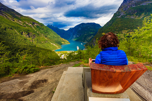 Tourism vacation and travel. Female tourist enjoying beautiful view over magical Geirangerfjorden from Flydalsjuvet viewpoint, Norway. Tourist attraction.