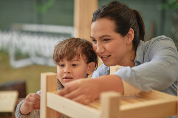 istock Young boy learning woodwork from his carpenter mom inside a class for child development. Male child and mother building a wooden chair to increase independence. Woman teaching her kid DIY 1410621242