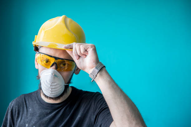 istock Caucasian guy, a worker in protective equipment (hardhat, eyewear, mask) holding a hardhat 1410626007