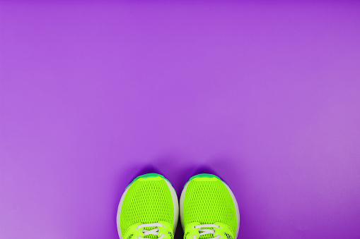 Green running shoes on a purple background. Top view, free space
