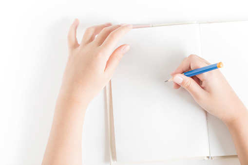 Hands of little kid hold the pencil and drawing on the blank book for creativity concept